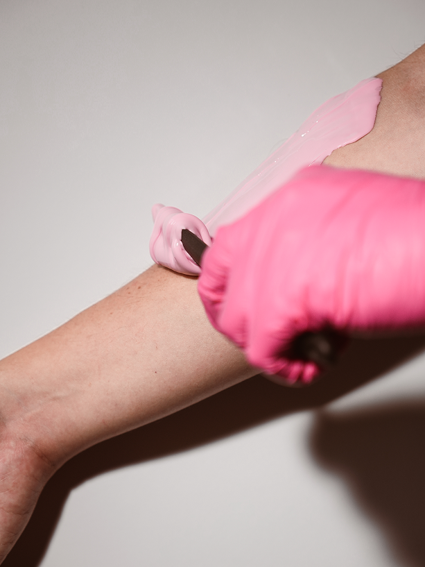 Pink Plumeria wax applied to a client's arm by a gloved esthetician