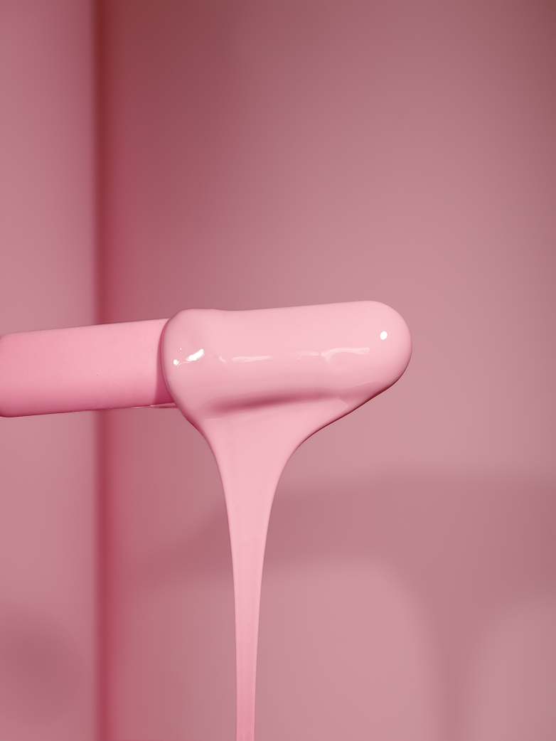 Glossy pink Plumeria hard wax stretching off a wooden spatula, showing its flexible professional-grade texture